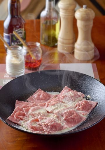 A vertical shot of pink salmon ravioli in a white sauce with mozzarella cheese on a deep black plate