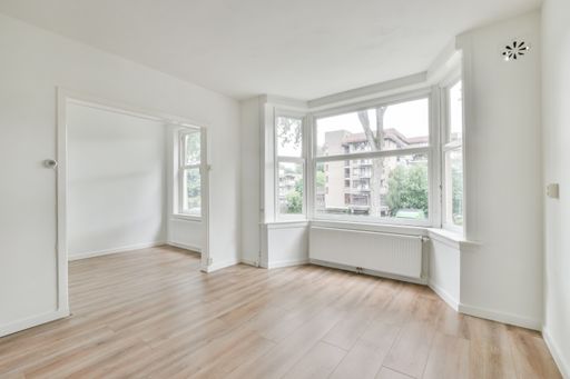 An interior shot of an empty room with white walls and a wooden floor with a nice window