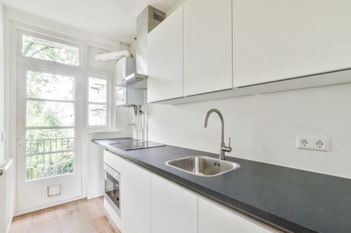 An interior shot of a modern kitchen in white tones next to a window