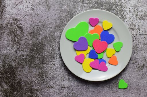 A top view shot of colorful heart-shaped cookies in a ceramic plate on a grey weathered surface