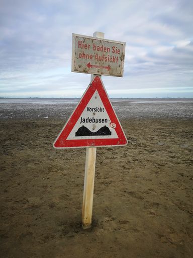 A warning sign on a wooden post saying "Swimming without supervision" at the beach of Dangast, Germany
