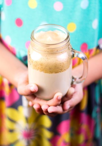 A vertical shot of a woman with colorful dress holding a caramel smoothie in her hands