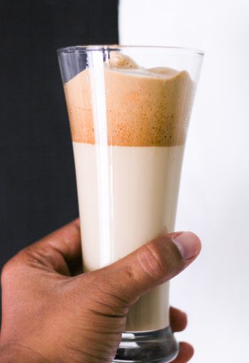 A vertical shot of a person holding a caramel smoothie behind a white and black background