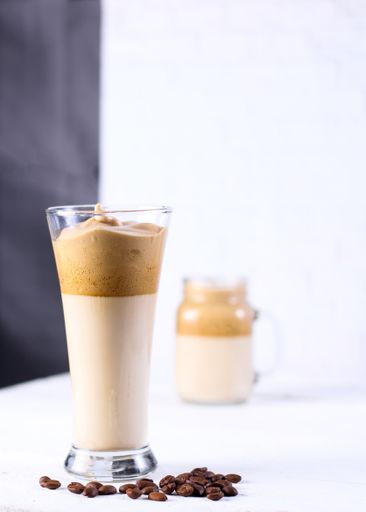 A vertical shot of two glasses of caramel smoothie next to each other surrounded by coffee beans