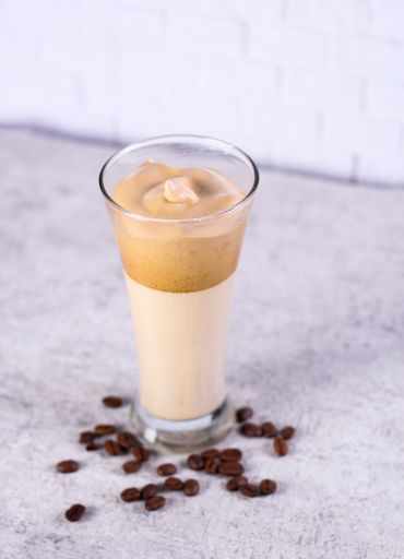 A vertical shot of a caramel smoothie surrounded by coffee beans on the table