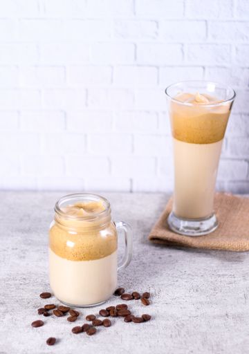 A vertical shot of two glasses of caramel smoothie next to each other surrounded by coffee beans