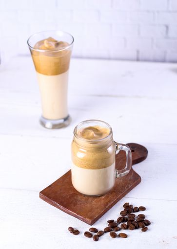 A vertical shot of caramel smoothie on a cutting board next to coffee beans behind another one
