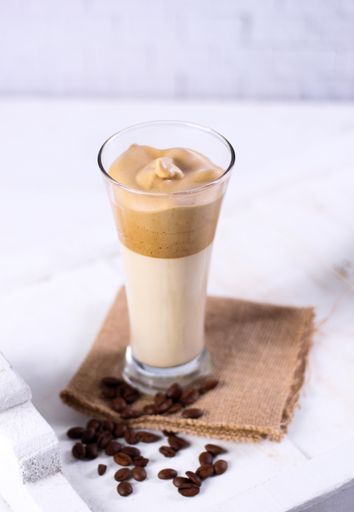 A vertical shot of a caramel smoothie on a brown napkin surrounded by coffee beans