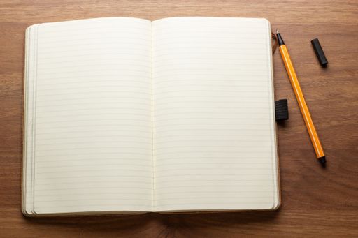 Open lined notebook with an orange pen on a wooden desk, perfect for writing or journaling concepts.