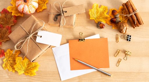 A top view shot of a wooden table with thanksgiving decors, envelopes, a gift box,and a pen