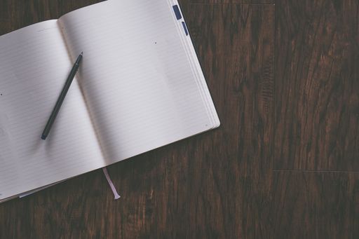 An overhead shot of an opened textbook with a ballpoint pen on it on a brown wooden background