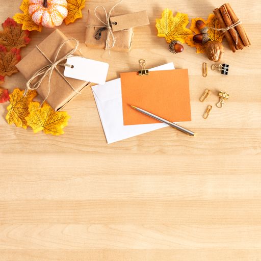 A top view shot of a wooden table with thanksgiving decors, envelopes,gift boxes, and a pen