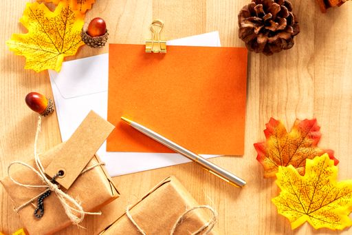 A top view shot of a wooden table with thanksgiving decors, envelopes, gift boxes, and a pen
