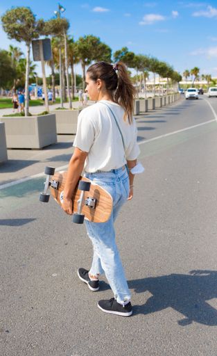 A side profile portrait of a young girl walking down the street with a skateboard and mask in the arm