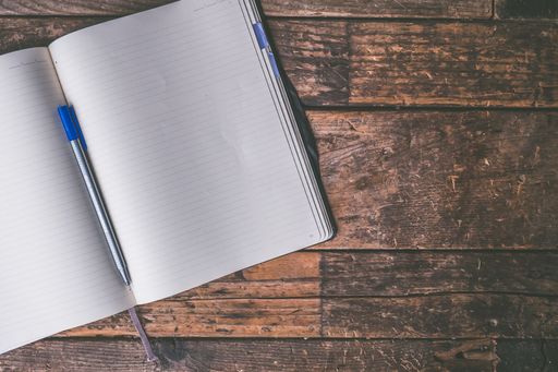 An overhead shot of an opened textbook with a ballpoint pen on it on a brown wooden background
