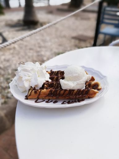 A vertical shot of homemade waffles with coconut ice cream, chocolate, and whipped cream on a table