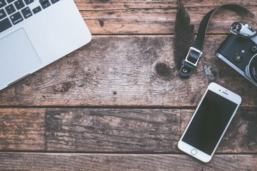 An overhead shot of a laptop, camera and a smartphone on a brown wooden background