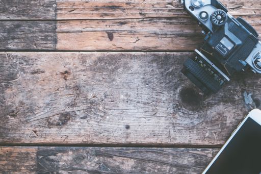 An overhead shot of a camera and a smartphone on a brown wooden background