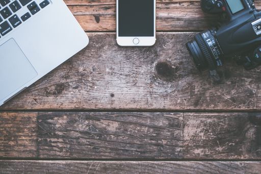 An overhead shot of a laptop, camera and a smartphone on a brown wooden background