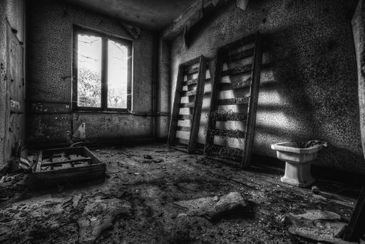 A grayscale shot of an empty room with old damaged furniture in an abandoned building
