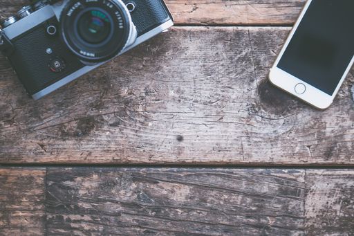 An overhead shot of a camera and a smartphone on a brown wooden background