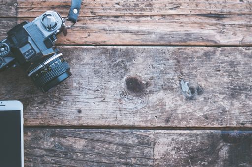 An overhead shot of a camera and a smartphone on a brown wooden background