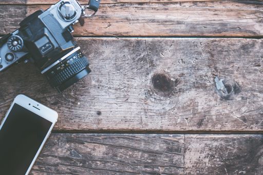 An overhead shot of a camera and a smartphone on a brown wooden background