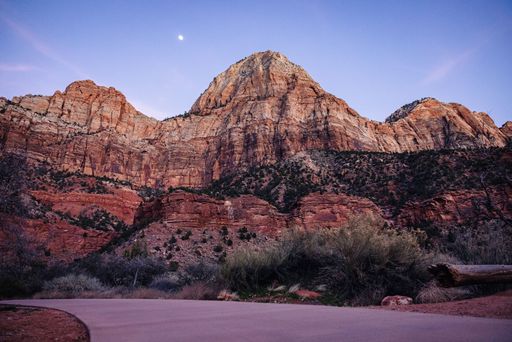 A stunning view of Zion National Park's red rock formations under a twilight sky with a visible moon.
