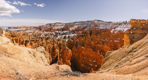 Panoramic view of Bryce Canyon's vibrant orange hoodoos under a clear blue sky with patches of snow, Utah, USA.