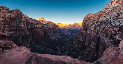 Scenic view of Zion Canyon with vibrant rock formations and a clear blue sky at sunset, highlighting the natural beauty of the landscape.