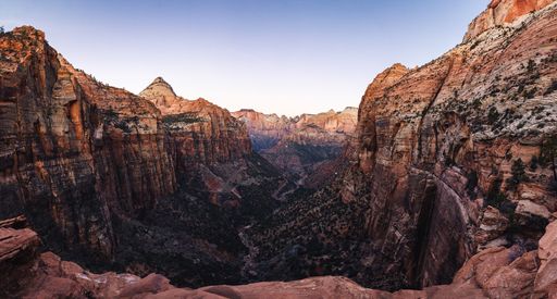 Panoramic view of Zion Canyon's stunning red rock formations under a clear sky at sunset.