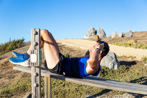Young Caucasian man doing exercises on public equipment in the outdoor gym at the park - doing abdominal crunches, with copy space