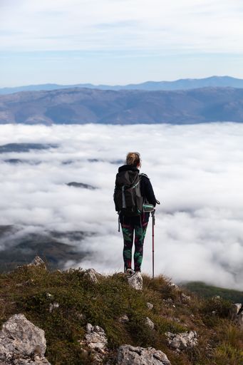 A vertical shot of the climber standing on the top of the mountain and looking at the clouds.