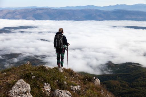 The climber standing on the top of the mountain and looking at the clouds.