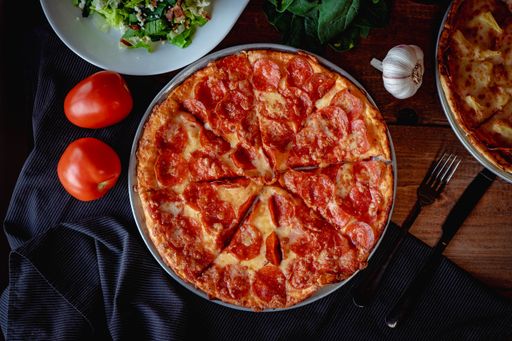 A closeup top view of a delicious pizza pepperoni and a salad  on a table with other ingredients