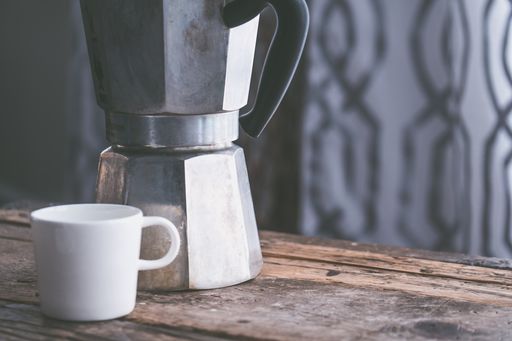 A closeup shot of a white ceramic cup next to a stainless metal kettle on a wooden surface