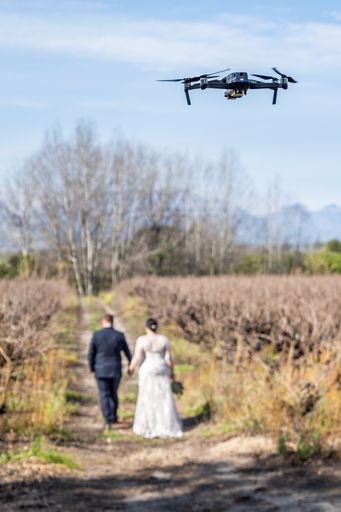 A vertical image of  a drone following a bridal couple during their wedding