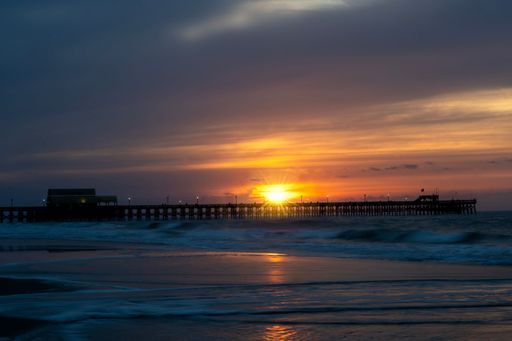 Sunset over a pier at Myrtle Beach, South Carolina, with vibrant sky and gentle waves, capturing the serene coastal beauty.