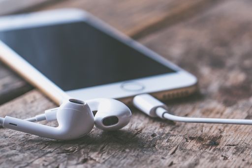 A closeup shot of a smartphone with connected headphones on a wooden surface