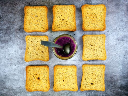 A top view of crispy toasted bread slices and a bowl of jam placed on a grey countertop background
