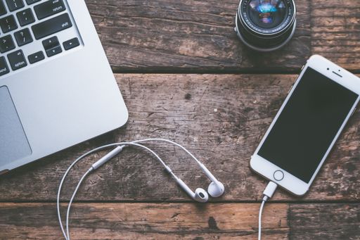 A closeup shot of a laptop with a smartphone and headphones on a wooden background and a camera lens