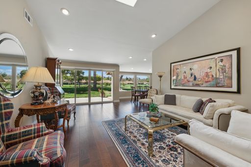 Spacious living room with elegant decor, large window view of a green garden, and a traditional painting on the wall.