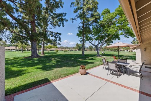 A patio with outdoor furniture overlooking a lush green golf course and trees under a clear blue sky.
