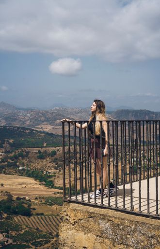 A vertical shot of a young woman standing on the terrace against the background of highlands.