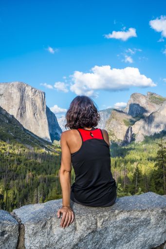 A vertical shot of a woman sitting on a rock in the Yosemite National Park in the USA