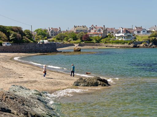 A couple walks along the wide sandy beach at Cemaes Bay, Anglesey, Wales.
