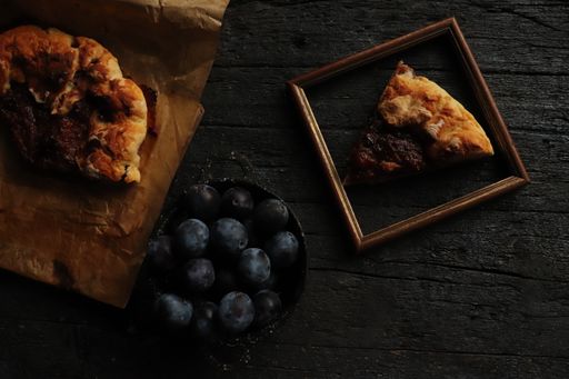 A top-view of fresh plums in a bowl and a pizza in a frame on a wooden rustic table
