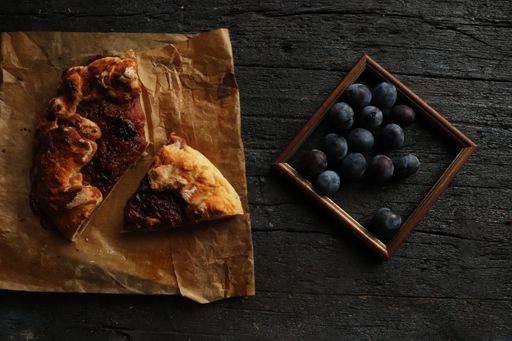 A top-view of fresh plums in a frame and a pizza on a wooden rustic table