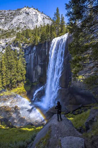 A vertical shot of a woman hiking in the Vernal Falls waterfall of Yosemite National Park in the USA