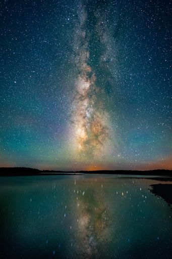 A vertical shot of the beautiful starry night sky above a lake and landscape